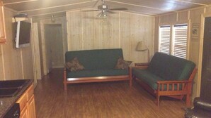 Un salon avec un canapé vert, une table basse en bois, un ventilateur de plafond et un plancher en bois.