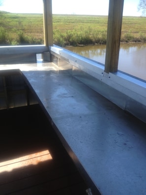 A room with a concrete floor, a wooden bench, and a view of a water body through large windows. - "Clean/Maintained Fully Furnished Lodging" -Speckled Trout (Buras)