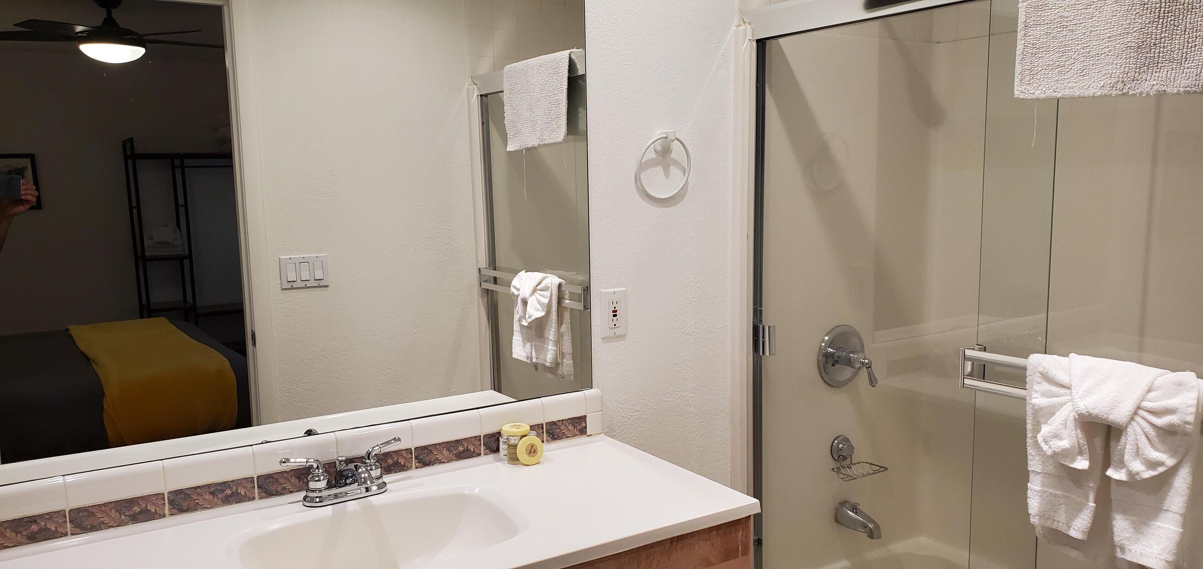 Une salle de bain avec un lavabo blanc, un miroir, une douche avec une porte en verre et un porte-serviettes.