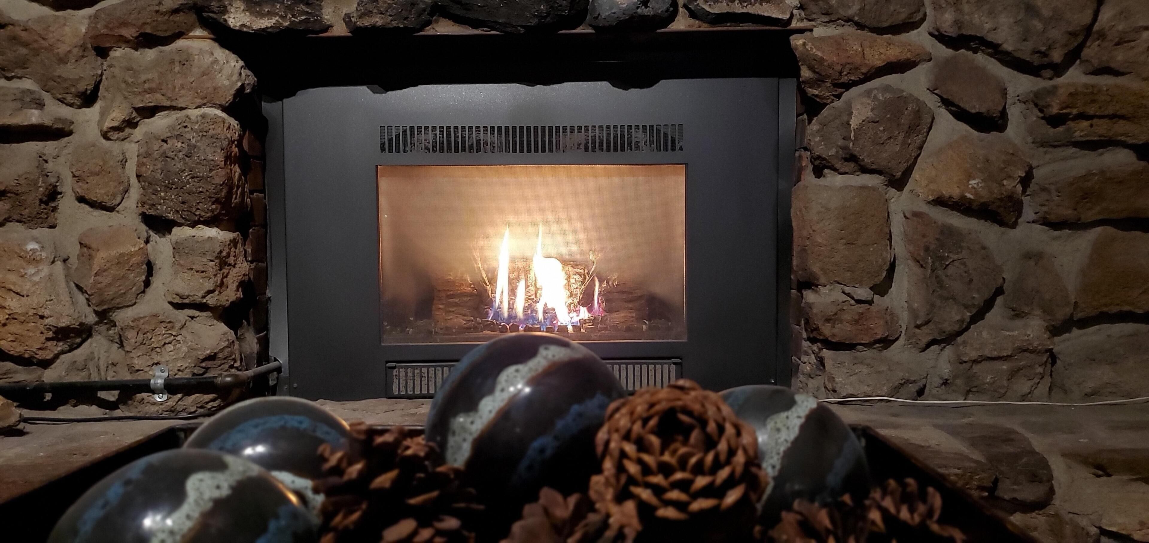 Una chimenea de piedra con fuego a la vista, rodeada de adornos como piñas y esferas de vidrio.