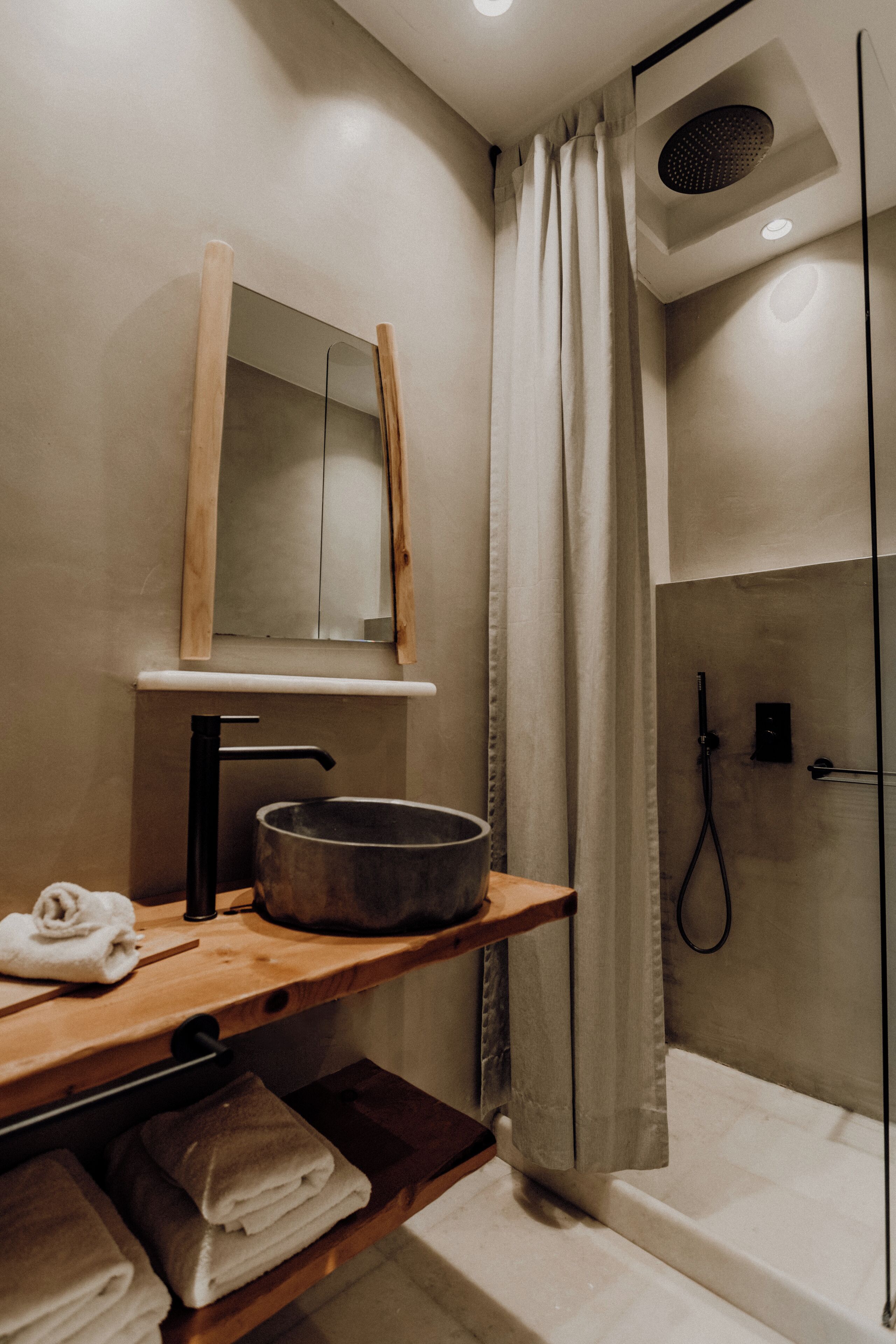 A modern bathroom with a wooden vanity, a large mirror, a black sink, and a shower area.