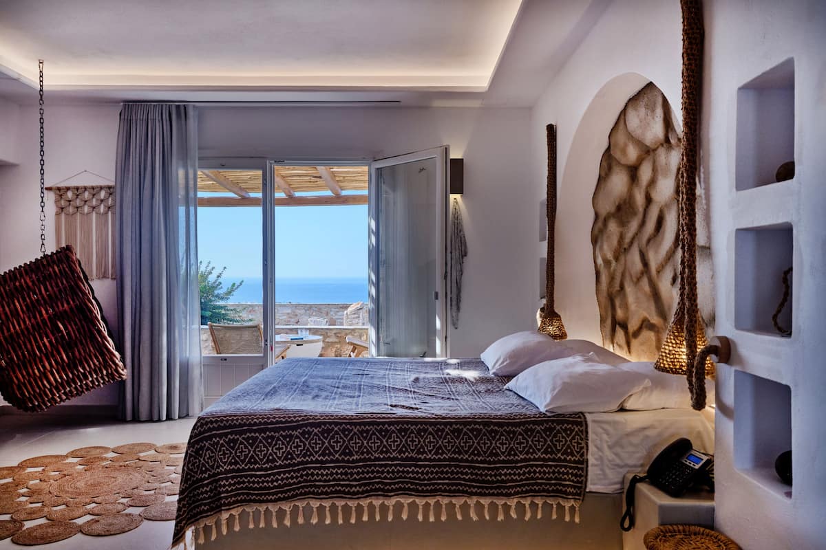 A modern bedroom with a large bed, a view of the sea, and a balcony.
