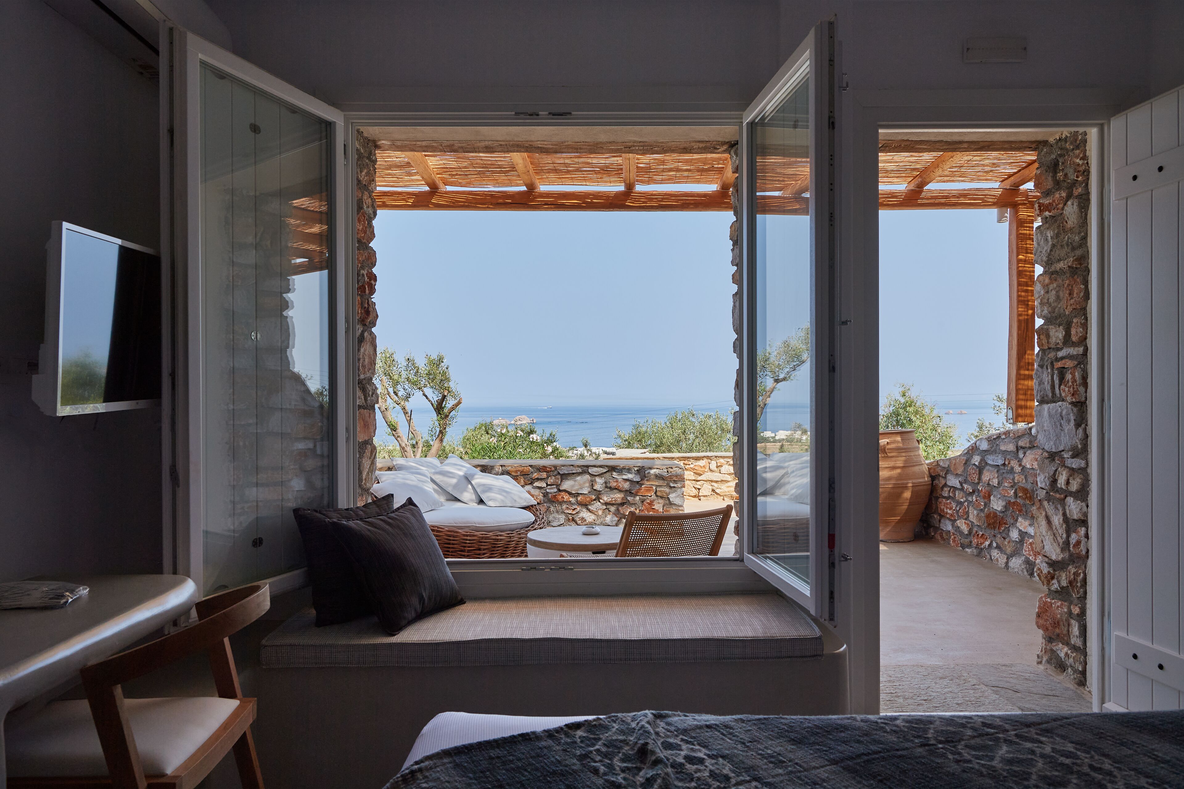 A balcony with a stone wall, a wooden pergola, and a view of the sea.