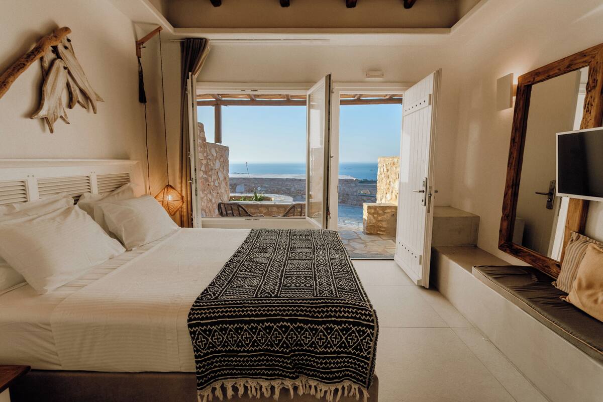 A bedroom with a bed, a large window, and a view of the sea.