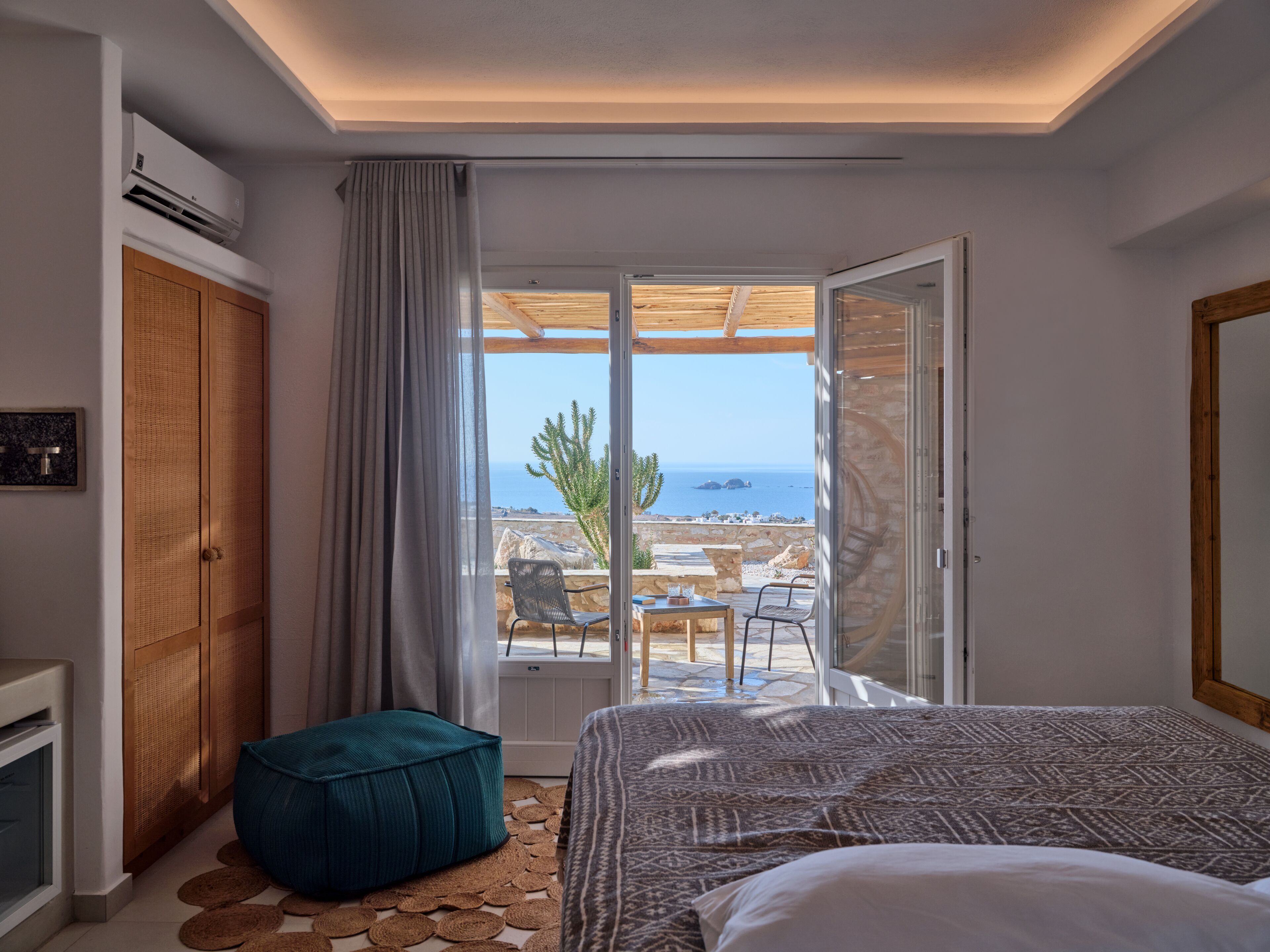 Quarto com cama, janela com vista para o mar, armário de madeira e ventoinha no teto.