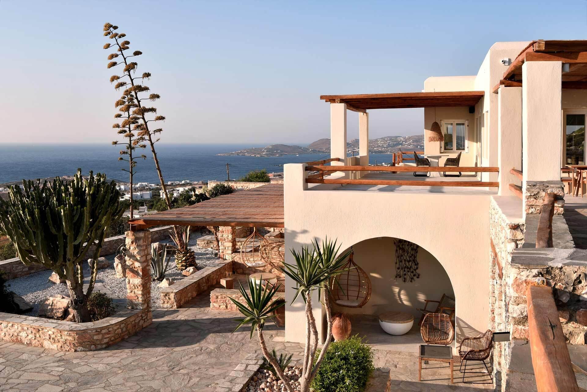 A Mediterranean-style villa with a terrace overlooking the sea, featuring stone walls, a wooden pergola, and outdoor seating.