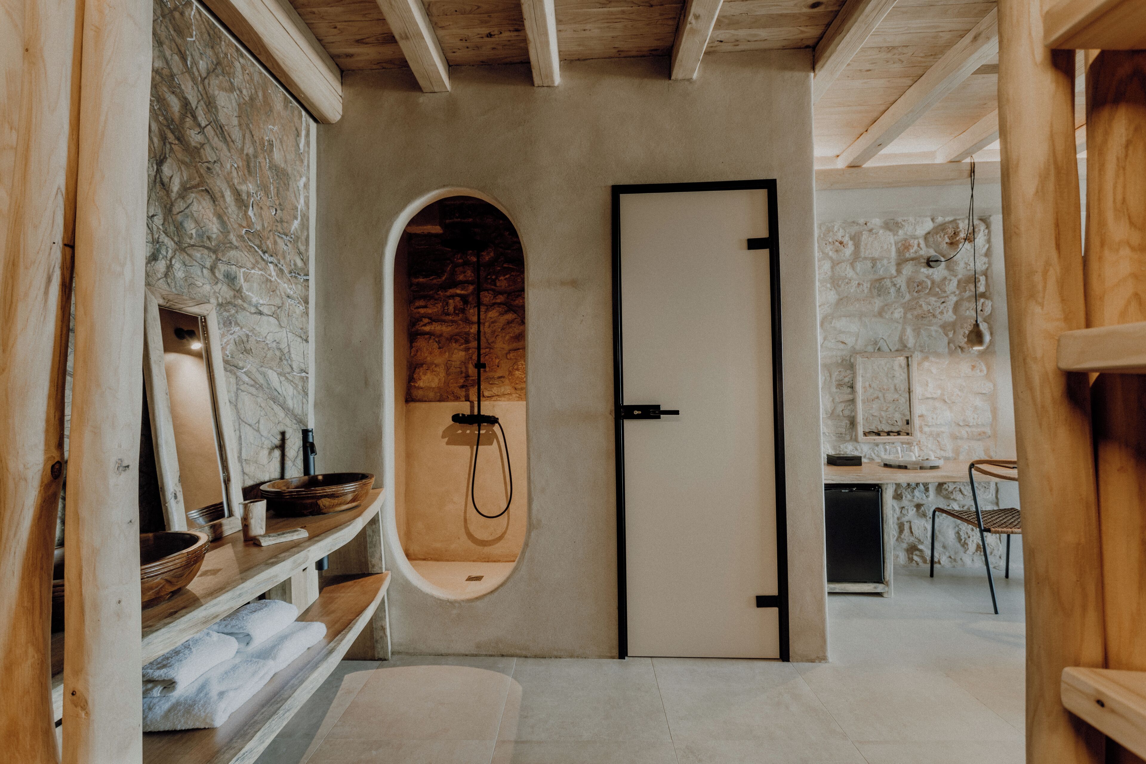 Une salle de bain avec un mur en pierre, un meuble-lavabo en bois et une cabine de douche.