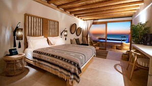 A bedroom with a large bed, wooden ceiling, and a view of the sunset through a large window. - Mythic Paros (Paros)