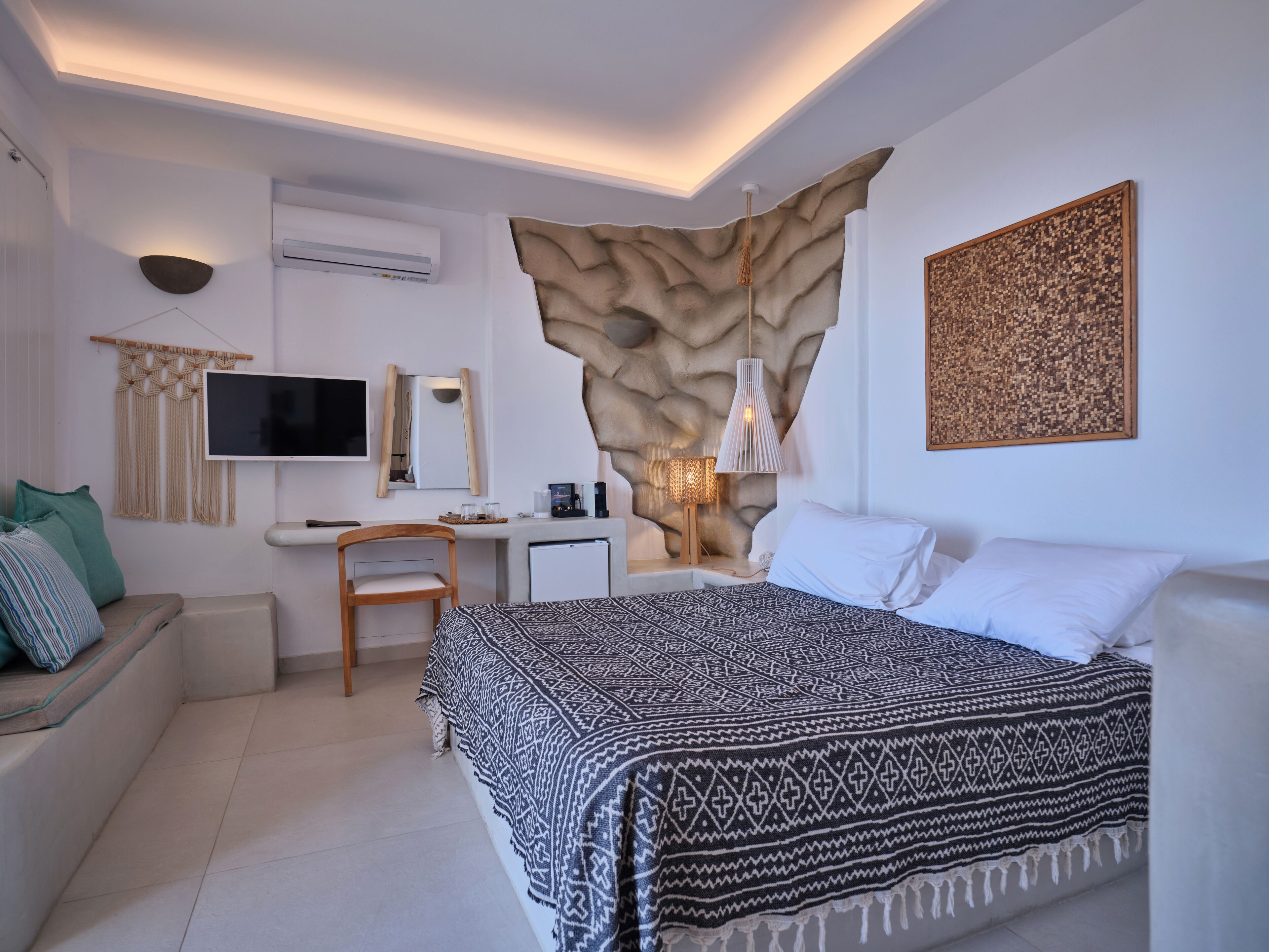 A modern bedroom with a bed, a desk, a chair, a TV, and a wall-mounted air conditioner.