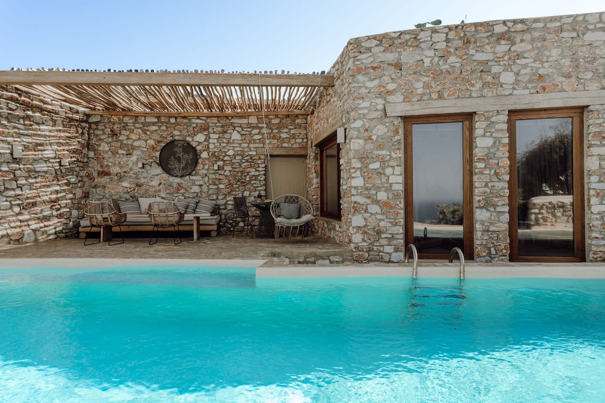 A stone building with a pool, outdoor seating, and a pergola.