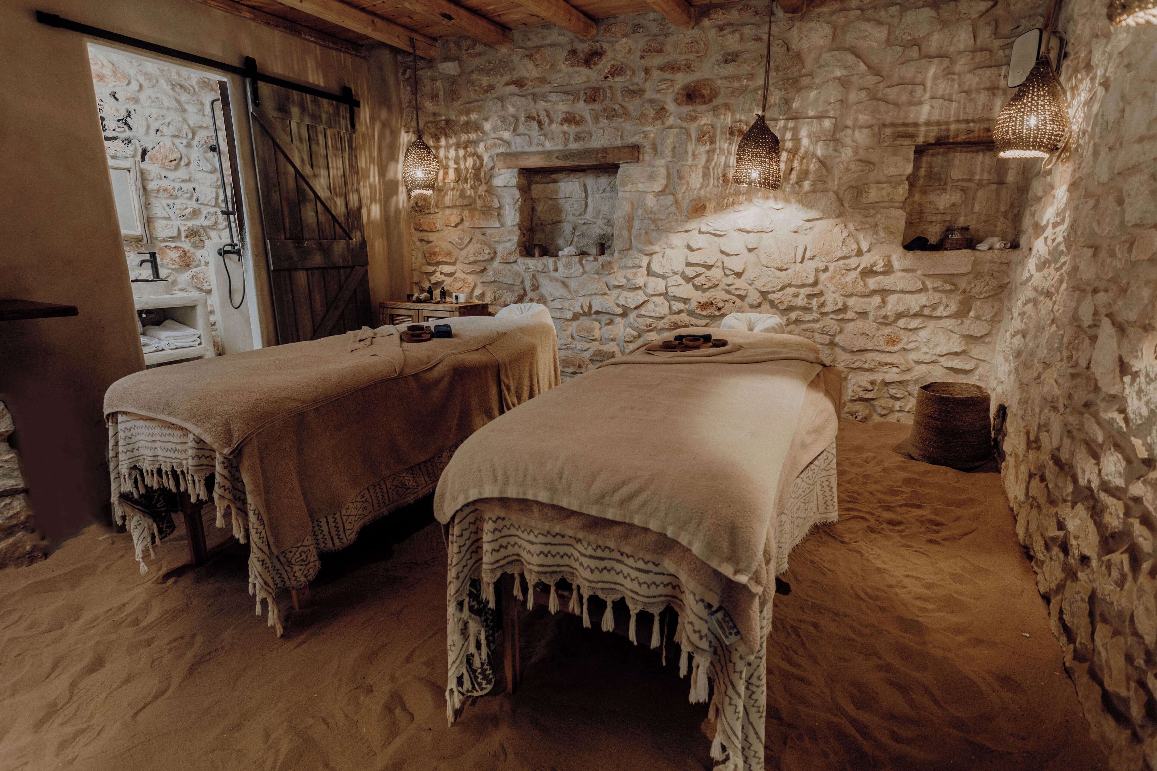 A rustic room with two beds, stone walls, a wooden ceiling, and hanging lights.