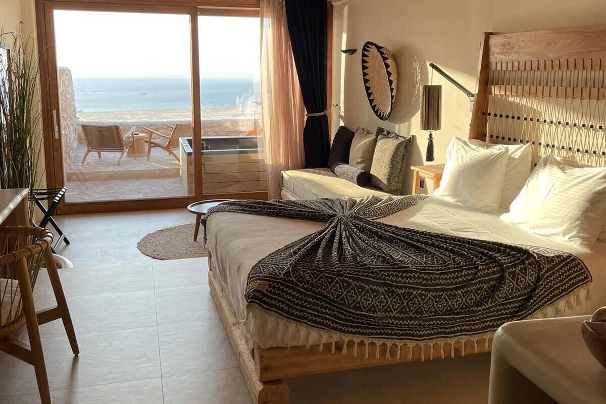 A bedroom with a bed, a desk, and a view of the sea.