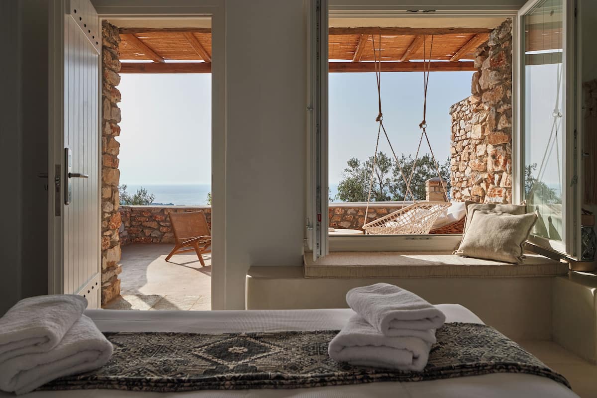 Una habitación con una cama, vistas al mar, una pared de piedra y un techo de madera.