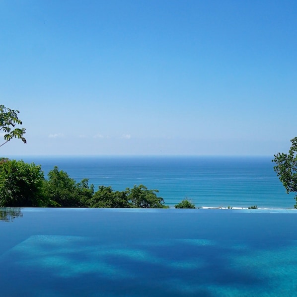 An infinity pool overlooking a clear blue ocean with a view of the horizon.