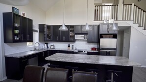 A modern kitchen with dark cabinets, a marble countertop, and bar stools. - Kinabik Cabin / Half block from beach, quiet cottage district (Sylvan Lake)