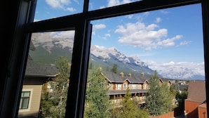 A view through a window of a mountain landscape with snow-capped peaks, a clear sky, and residential buildings in the foreground.