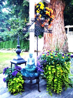 Ein Garten mit einer Statue, einem dekorativen Metallständer und einem großen Baum.