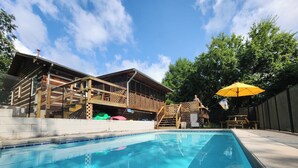A swimming pool with a wooden deck and a covered area with a yellow umbrella. - Log home on 50 acres. Private, convenient, beautiful. A little bit of paradise. (Knoxville)
