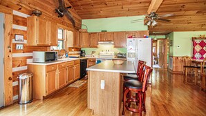 A wooden cabin kitchen with a central island, wooden cabinets, and a ceiling fan. - Log home on 50 acres. Private, convenient, beautiful. A little bit of paradise. (Knoxville)