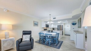 A modern kitchen with white cabinets, a dining area with blue chairs, and a black leather chair.