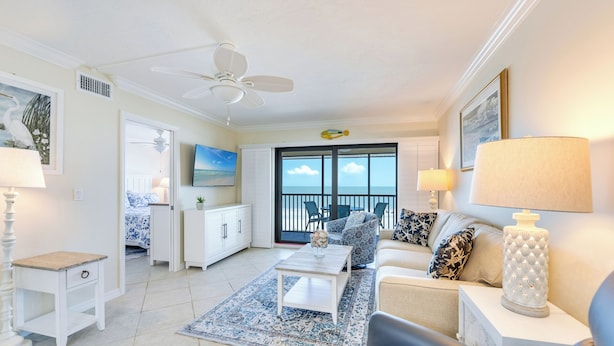 A spacious living room with a ceiling fan, a large window with a view, a white sofa, a coffee table, and a dining area with chairs and a table.