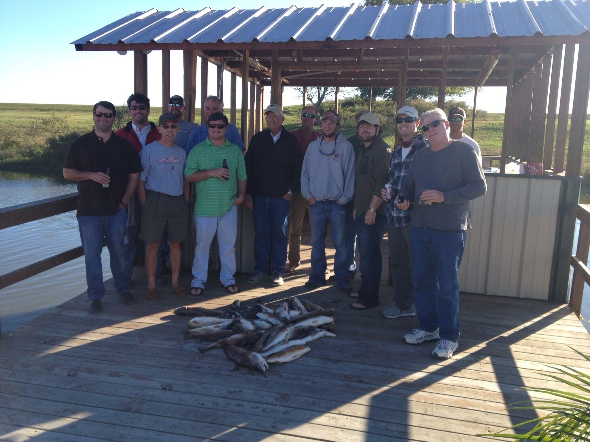 A group of people standing on a wooden deck with a metal roof, overlooking a body of water.