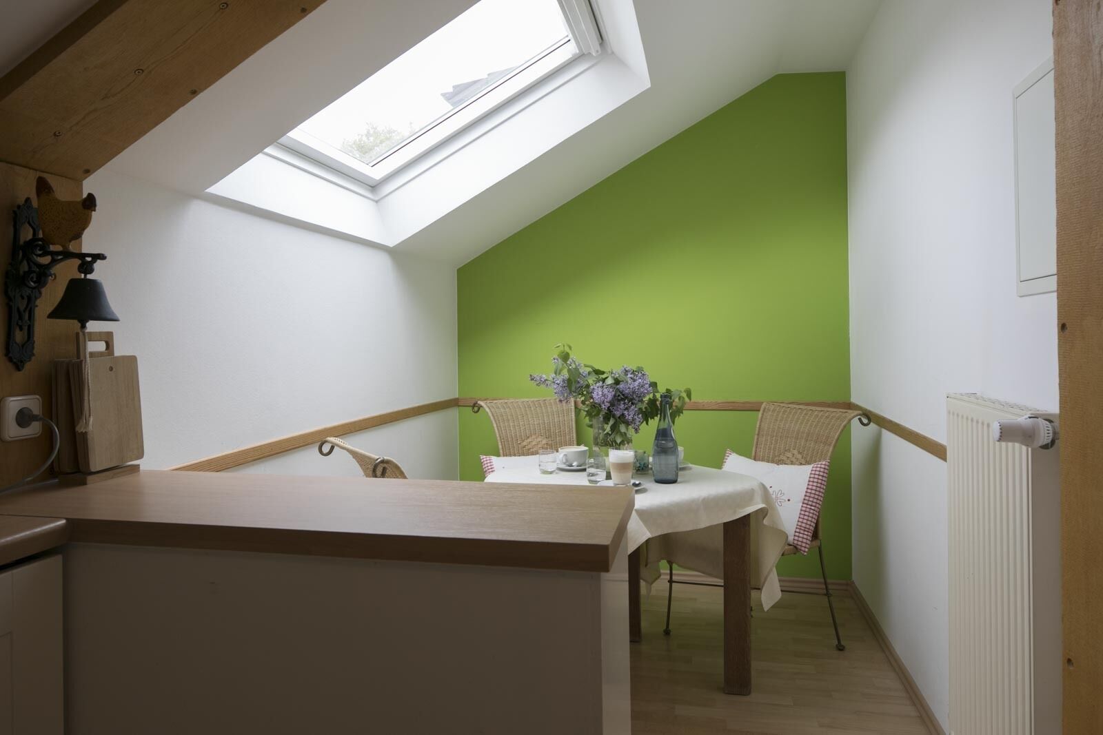 A cozy corner with a table set for two, a green wall, and a skylight above.