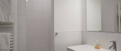 A modern bathroom with white tiles, a glass shower enclosure, a vanity with a mirror, and a towel rack.