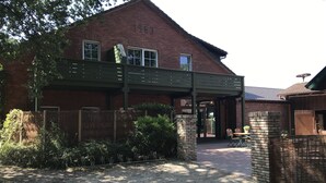 A brick building with a covered walkway, a brick chimney, and a gravel driveway. - Landcafé Neumann (Bad Zwischenahn)