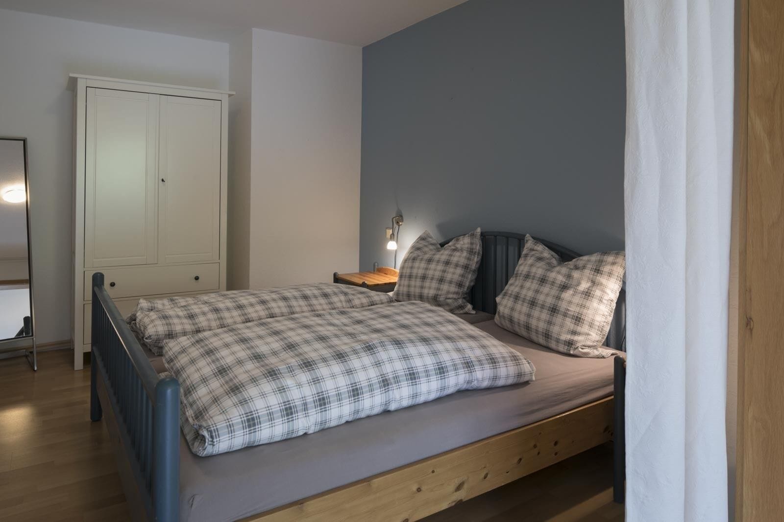 A bedroom with a bed, a nightstand, a lamp, and a wardrobe.