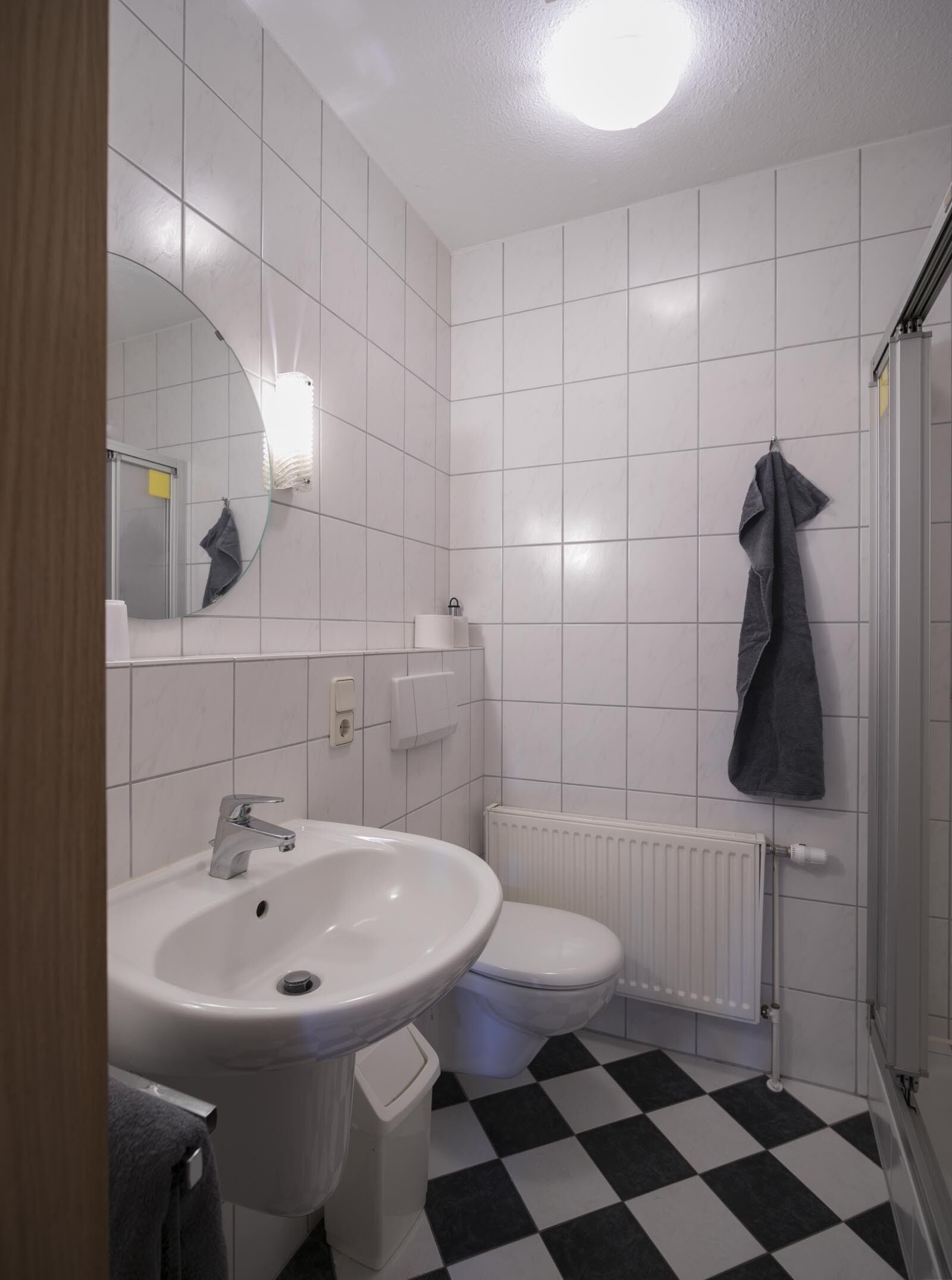 Un baño con un lavamanos blanco, inodoro y espejo. Hay una toalla colgada en la pared y un radiador debajo del inodoro.