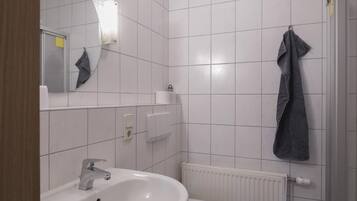 Un baño con un lavamanos blanco, inodoro y espejo. Hay una toalla colgada en la pared y un radiador debajo del inodoro.