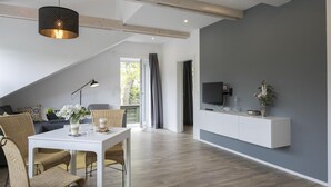 A modern living room with a dining area, a TV mounted on a grey wall, and a balcony with curtains. - Landcafé Neumann (Bad Zwischenahn)