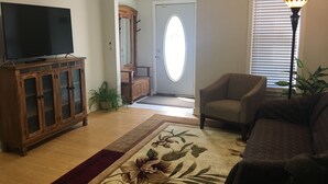 A living room with a TV on a wooden cabinet, a floral rug, a sofa, a chair, a potted plant, and a lamp.