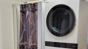 A laundry room with two stacked front-loading washing machines and a wooden door with a curtain.