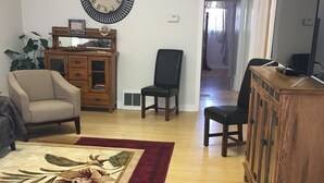 A living room with a wooden cabinet, a black chair, a beige armchair, a large clock, and a floral rug.