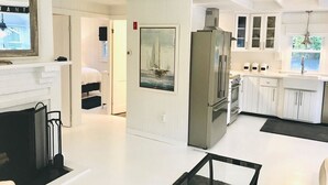 A modern kitchen with white cabinetry, a stainless steel refrigerator, and a dining area with a glass table. - Renovated cottage 1 mile to beach in Chatham! (Chatham)