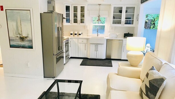 A modern kitchen with white cabinets, stainless steel appliances, and a dining area with a white table and sofa. - Renovated cottage 1 mile to beach in Chatham! (Chatham)