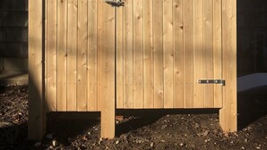 A wooden gate with a metal latch, set against a building with a brick wall and a window. - Renovated cottage 1 mile to beach in Chatham! (Chatham)