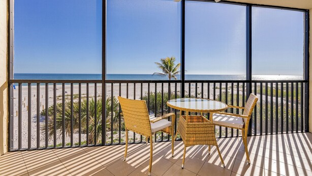 A balcony with a view of the beach, featuring wicker furniture and a ceiling fan. - OCEAN'S REACH 4B3: 3rd Floor, Gorgeous Gulf-Front Views, Amenities Open! (Sanibel Island)