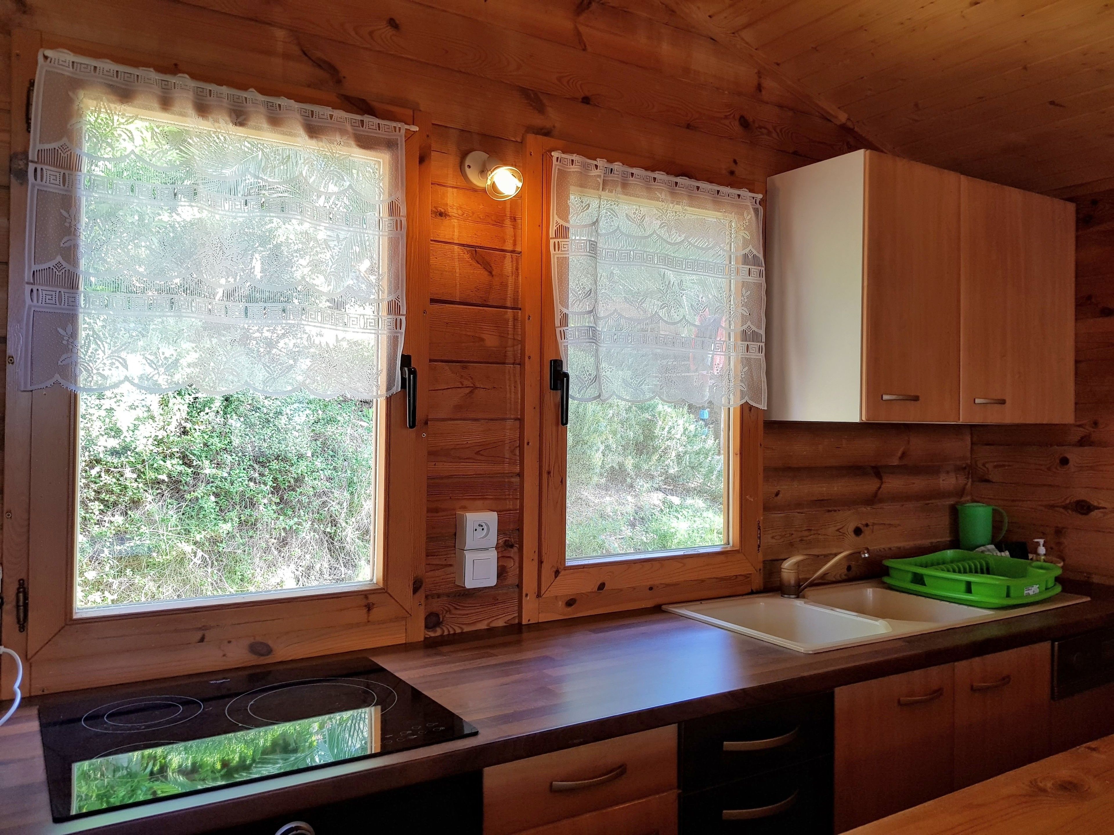 Cocina de cabaña de madera con dos ventanas grandes, una estufa, un fregadero y armarios de madera.