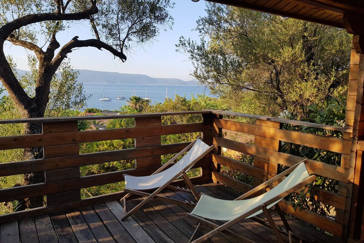 A wooden deck with a hammock chair and a wooden railing overlooking a body of water with boats.