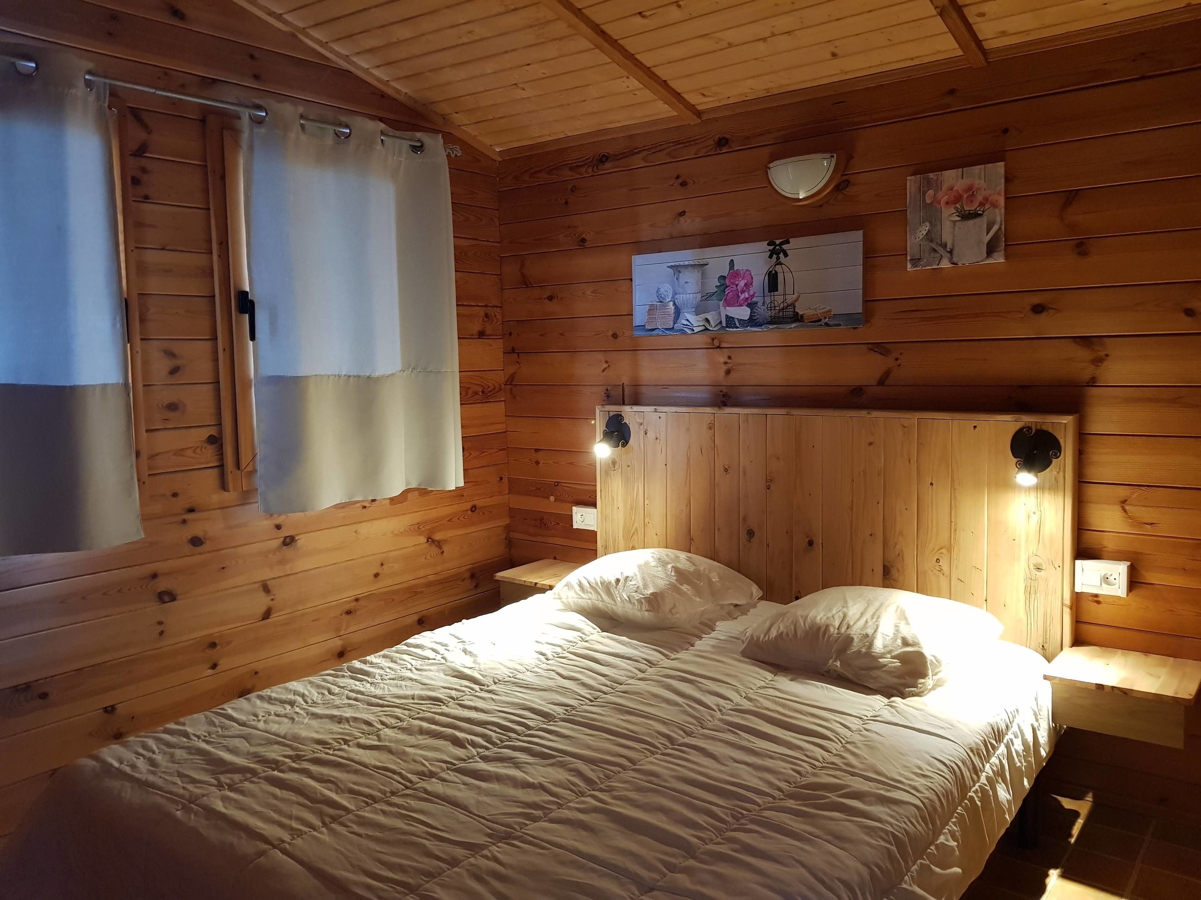 Une pièce de style cabane en bois, avec un lit, des rideaux, une lampe fixée au mur et un tableau.