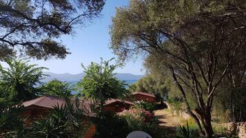 Un patio con mesa y sillas, rodeado de árboles y vistas al mar y a las montañas.