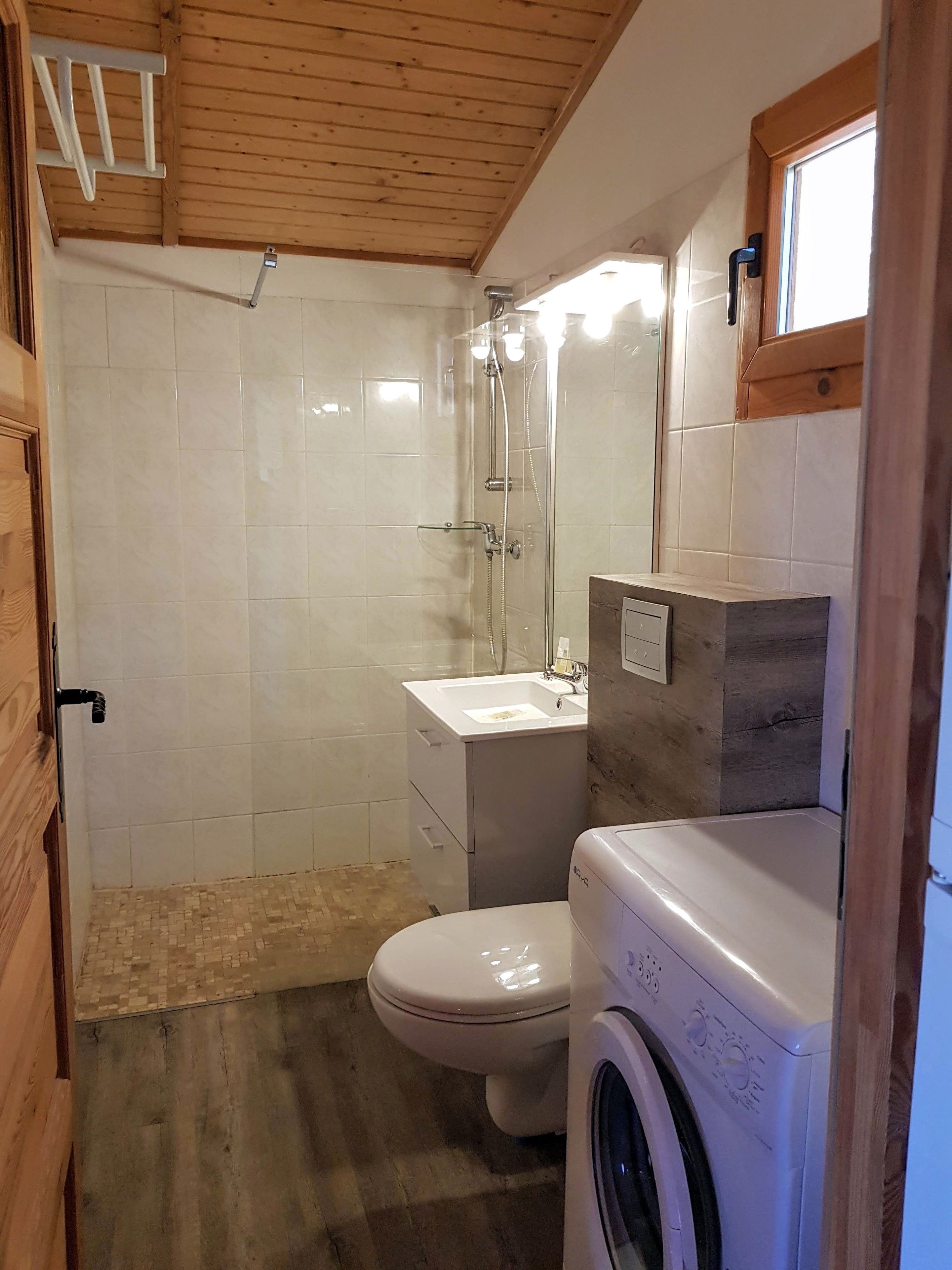 A compact bathroom with a shower, toilet, and washing machine.