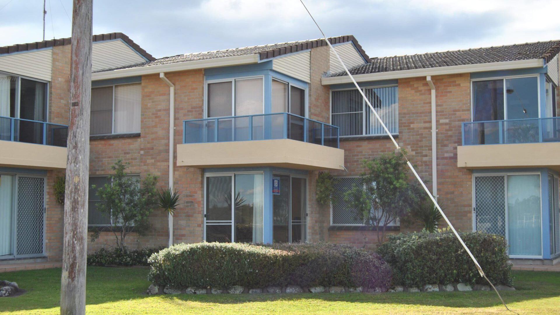 A multi-story residential building with a brick facade, large windows, and a balcony on the second floor.