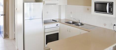 Een keuken met witte kastjes, een roestvrijstalen koelkast, een magnetron, een fornuis en een spoelbak.