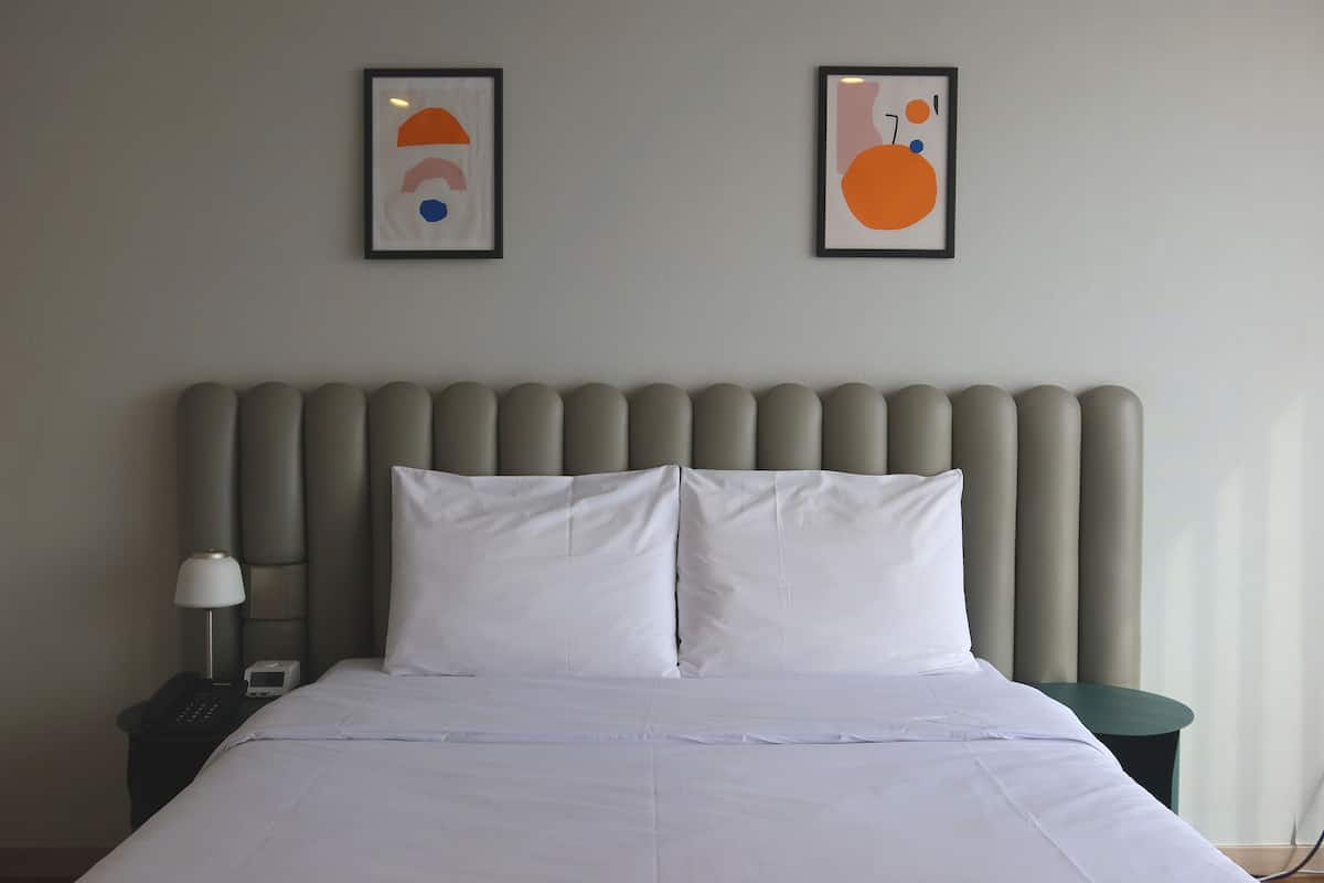 A hotel room with a bed, a nightstand with a lamp, and two framed abstract artworks on the wall.