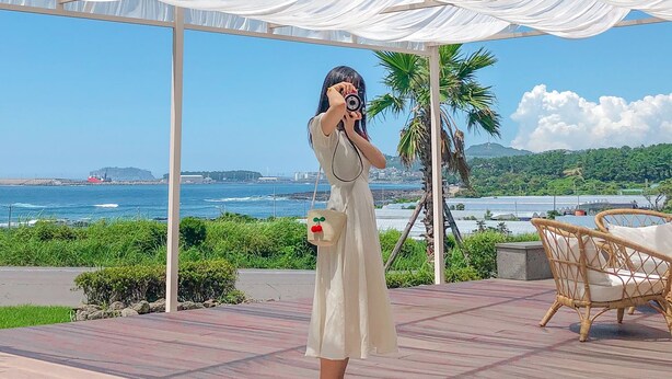 A person taking a photo under a white canopy with a coastal view in the background. - Hotel Seogwipean (Seogwipo)