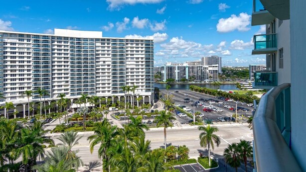 A high-rise hotel with multiple floors, a parking lot, and palm trees. - Beachfront Apt | Hollywood, 10th Floor + Pool (Hollywood)